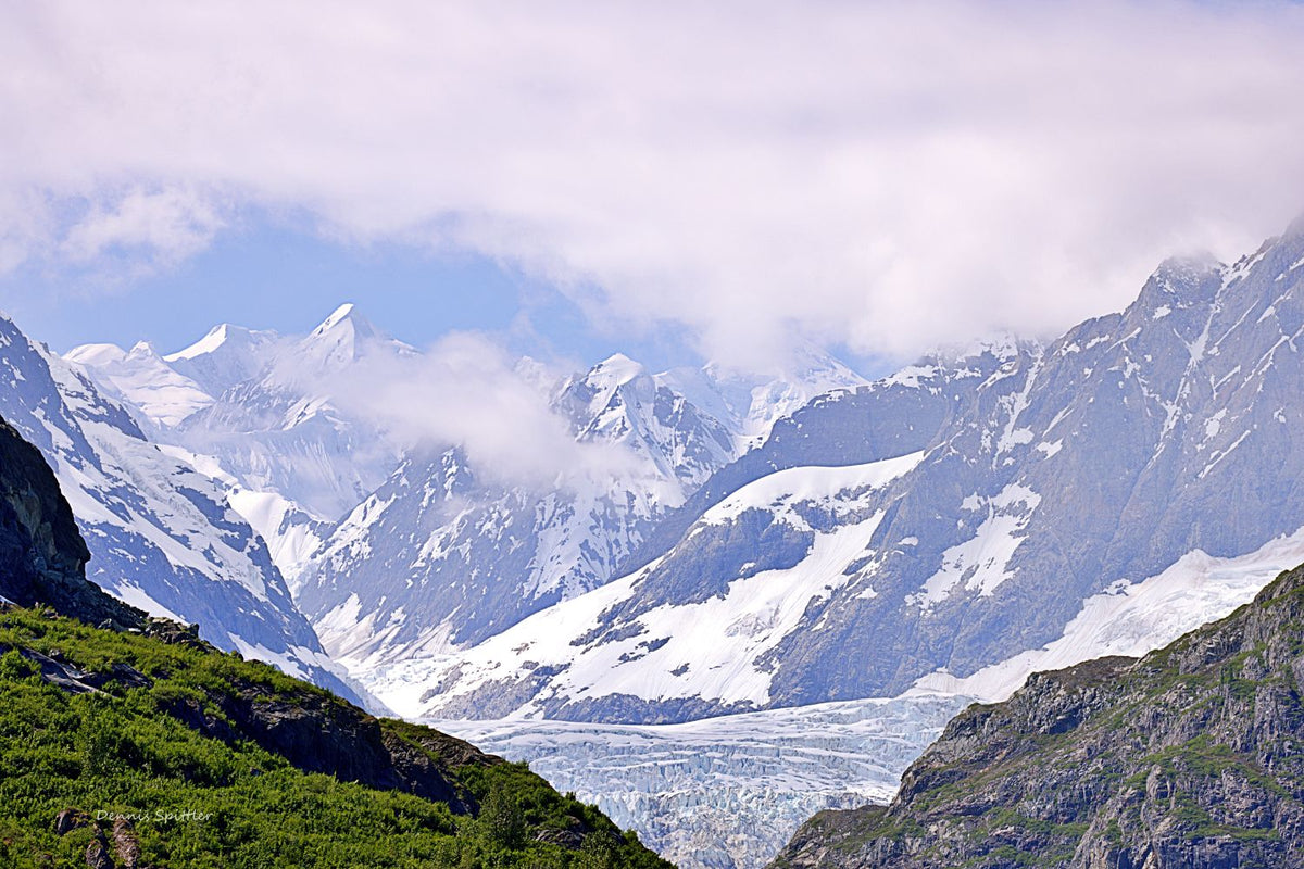 Dramatic Alaska glacier valley with snow-capped peaks and glacier flowing between mountains with green tundra foreground